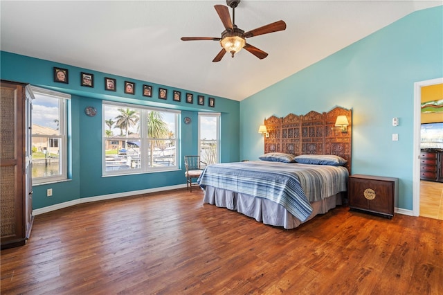 bedroom featuring lofted ceiling, multiple windows, baseboards, and wood finished floors