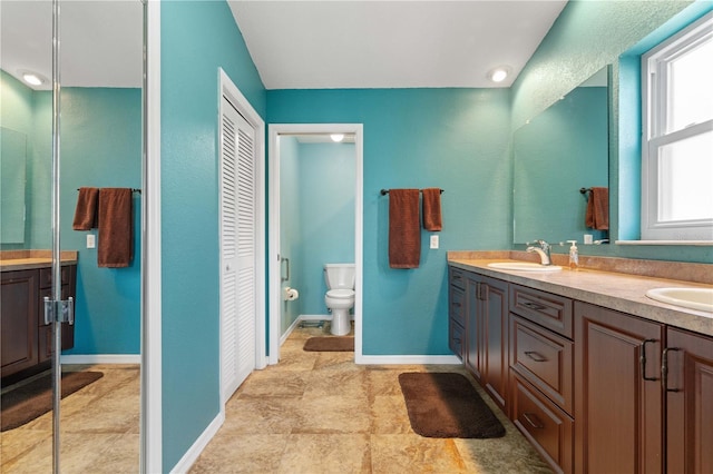 bathroom featuring double vanity, a closet, baseboards, toilet, and a sink