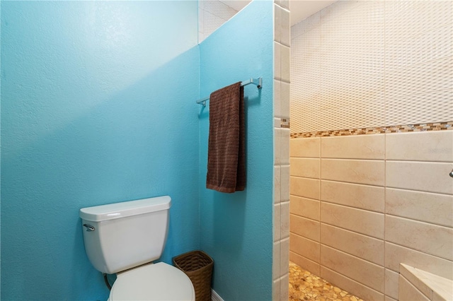 full bath with a textured wall, tiled shower, and toilet