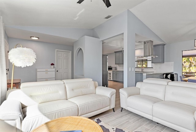 living area featuring lofted ceiling, visible vents, a ceiling fan, and wood finish floors