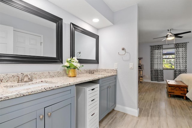 bathroom with double vanity, a ceiling fan, a sink, wood finished floors, and baseboards