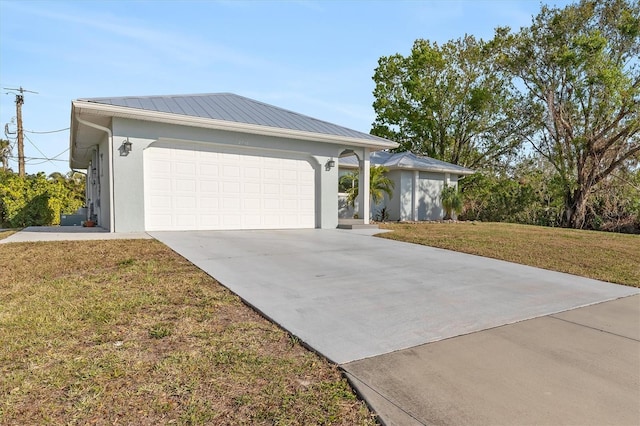 ranch-style home featuring driveway, a garage, metal roof, a front lawn, and stucco siding