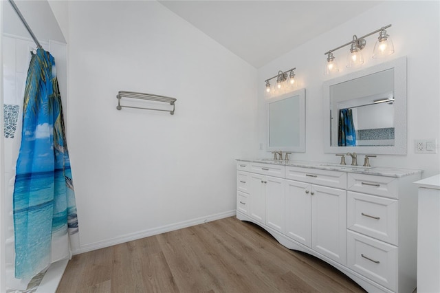 bathroom with vaulted ceiling, double vanity, wood finished floors, and a sink