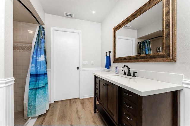 full bathroom with visible vents, tiled shower, wood finished floors, and vanity