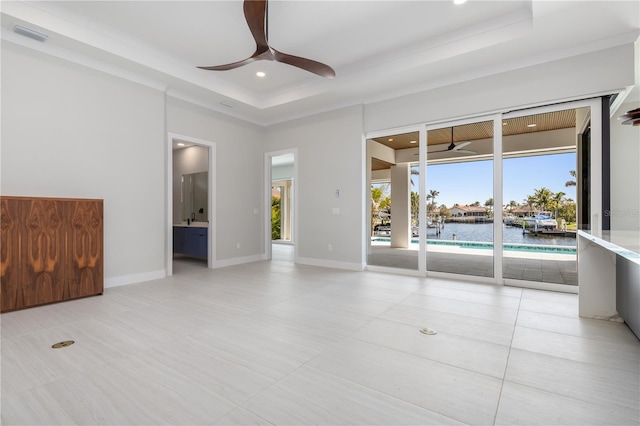 spare room with a tray ceiling, a water view, a ceiling fan, and baseboards