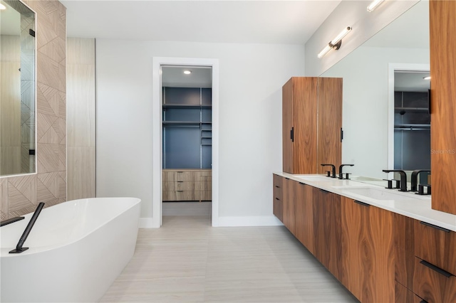 full bathroom with a walk in closet, double vanity, a freestanding bath, a sink, and baseboards