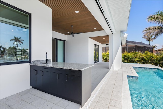 view of patio with an outdoor kitchen, outdoor wet bar, a sink, a ceiling fan, and an outdoor pool