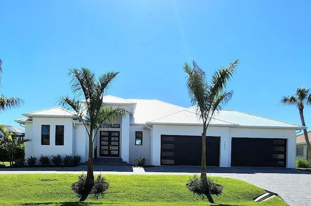 view of front of house featuring stucco siding, french doors, decorative driveway, a front lawn, and a garage