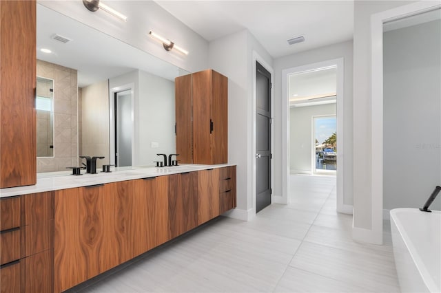 full bath featuring baseboards, double vanity, a soaking tub, visible vents, and a sink