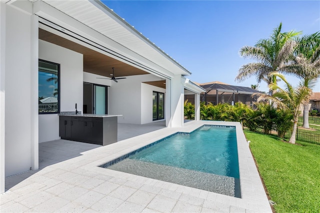 view of swimming pool featuring a patio area, a sink, exterior kitchen, a ceiling fan, and a fenced in pool