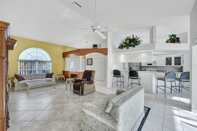 living room featuring arched walkways, light tile patterned floors, visible vents, ceiling fan, and high vaulted ceiling