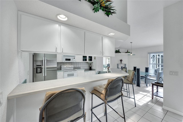 kitchen with a peninsula, white appliances, a sink, white cabinets, and light countertops