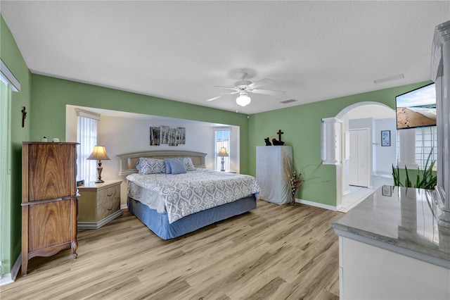 bedroom featuring arched walkways, visible vents, baseboards, a ceiling fan, and light wood-type flooring