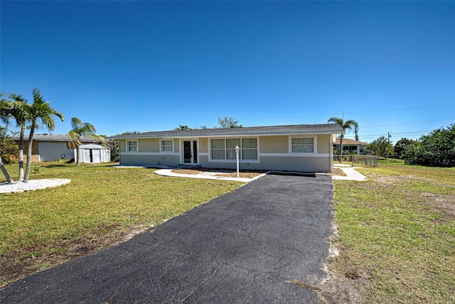 single story home with an outbuilding, stucco siding, a front lawn, a storage unit, and aphalt driveway