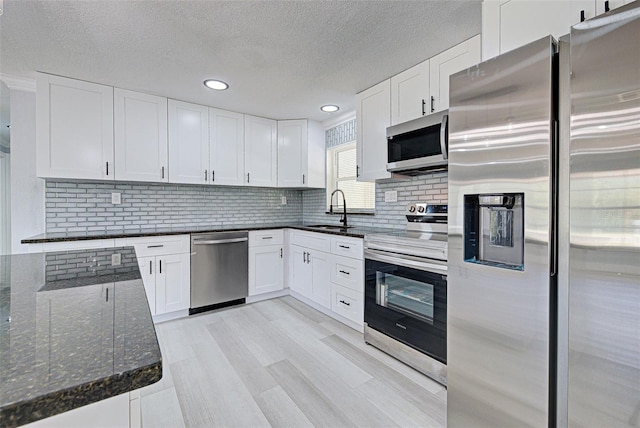 kitchen with a sink, tasteful backsplash, dark stone counters, appliances with stainless steel finishes, and white cabinets