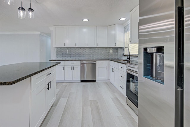 kitchen featuring a sink, tasteful backsplash, stainless steel appliances, light wood-style floors, and white cabinets