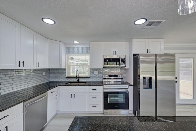 kitchen with visible vents, a sink, white cabinetry, stainless steel appliances, and dark stone counters