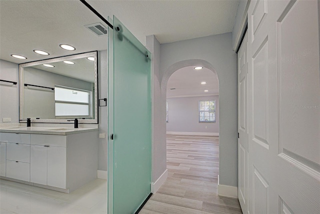 bathroom featuring wood finished floors, visible vents, baseboards, double vanity, and recessed lighting