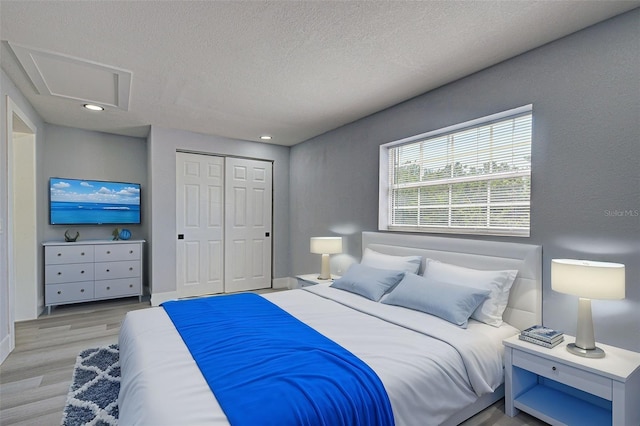 bedroom featuring light wood-type flooring, a textured ceiling, a closet, baseboards, and attic access