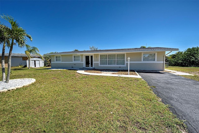 ranch-style home with a front lawn, aphalt driveway, an outdoor structure, and stucco siding