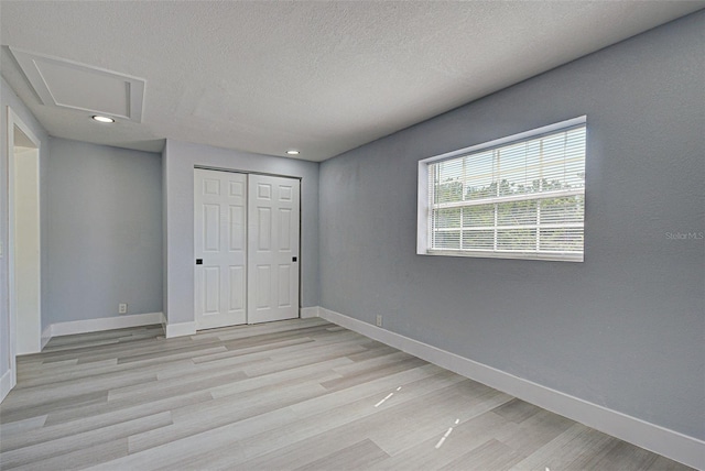 unfurnished bedroom featuring baseboards, attic access, light wood-style flooring, a closet, and a textured ceiling