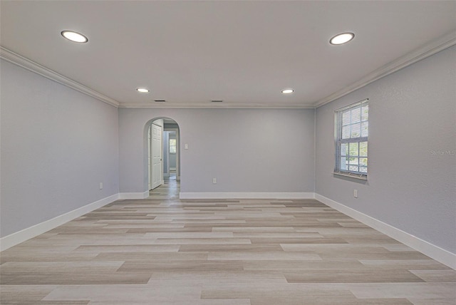 spare room featuring light wood finished floors, baseboards, ornamental molding, recessed lighting, and arched walkways