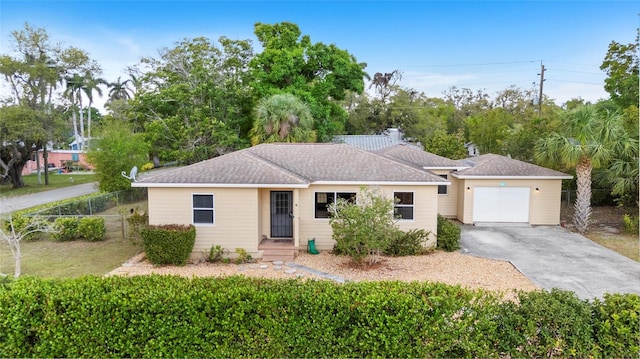 single story home featuring driveway, a shingled roof, an attached garage, and fence