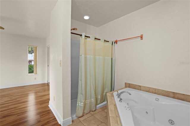 bathroom featuring a stall shower, a jetted tub, baseboards, and wood finished floors