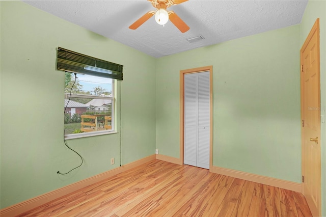 unfurnished room featuring baseboards, visible vents, ceiling fan, wood finished floors, and a textured ceiling