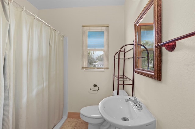 bathroom with a shower with curtain, toilet, a sink, tile patterned flooring, and baseboards