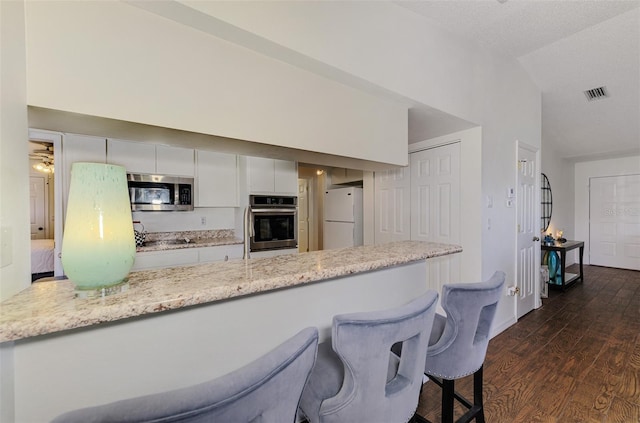 kitchen with visible vents, white cabinets, dark wood finished floors, vaulted ceiling, and stainless steel appliances