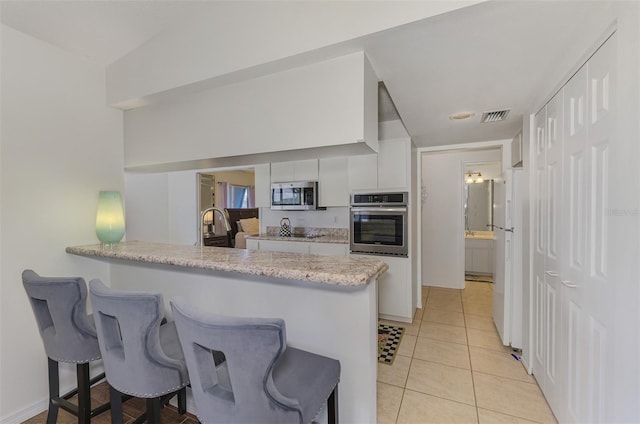 kitchen featuring light tile patterned floors, visible vents, appliances with stainless steel finishes, white cabinetry, and a kitchen bar