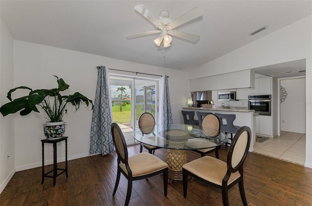 dining space featuring ceiling fan, wood finished floors, visible vents, baseboards, and vaulted ceiling