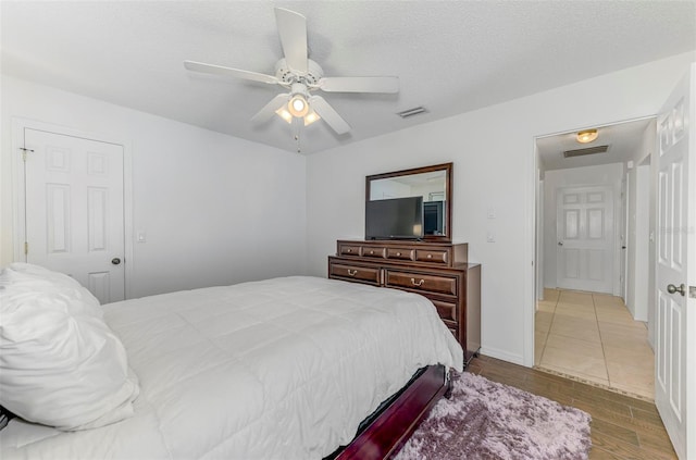 bedroom with a ceiling fan, visible vents, a textured ceiling, and wood finished floors