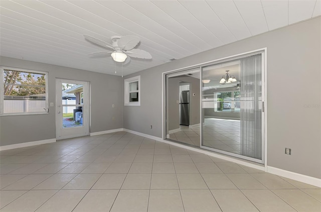 unfurnished room featuring baseboards, ceiling fan with notable chandelier, and light tile patterned flooring