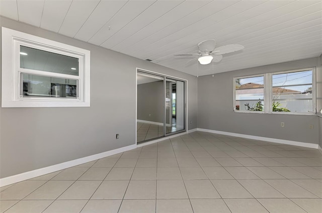 empty room with light tile patterned flooring, a ceiling fan, and baseboards