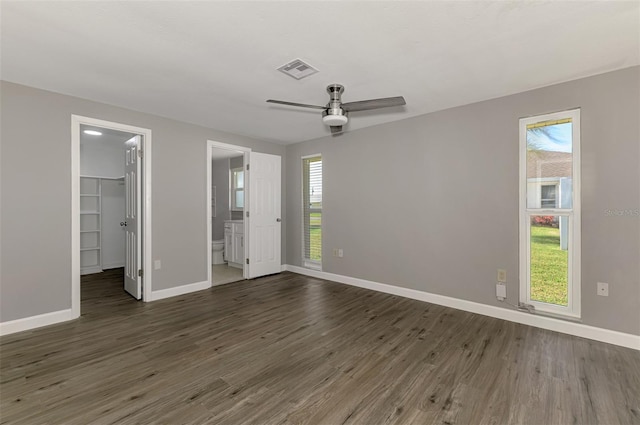 unfurnished bedroom featuring baseboards, visible vents, dark wood-style flooring, a walk in closet, and multiple windows