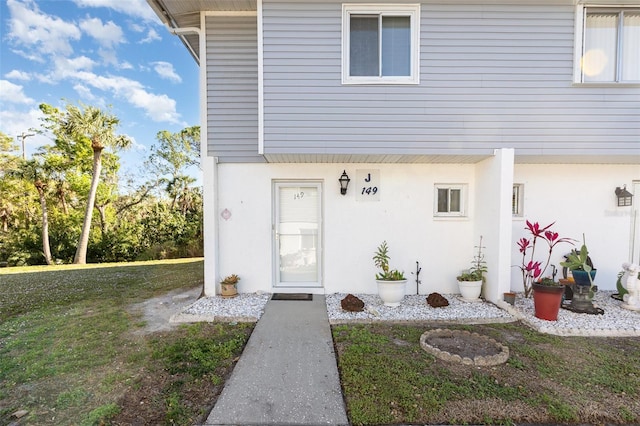 view of exterior entry featuring a lawn and stucco siding