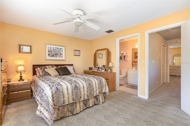 carpeted bedroom featuring visible vents, baseboards, ceiling fan, ensuite bathroom, and a textured ceiling