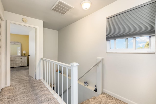 hallway featuring visible vents, an upstairs landing, and carpet