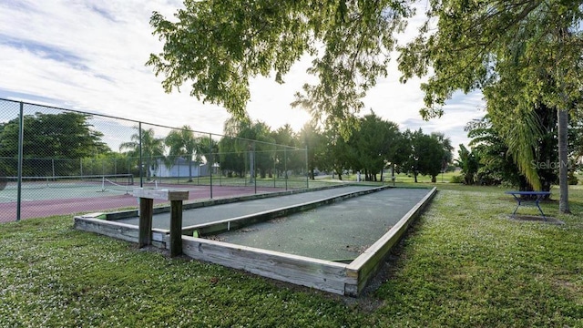 view of property's community with a yard, a tennis court, and fence