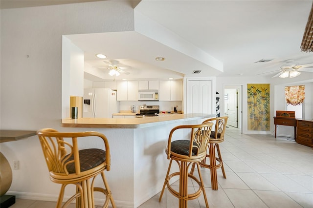 kitchen featuring white appliances, a ceiling fan, a kitchen breakfast bar, a peninsula, and light countertops