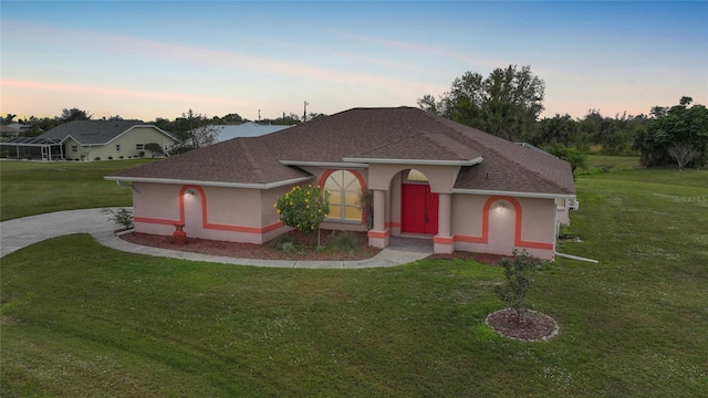 view of front of house featuring a yard, roof with shingles, and stucco siding