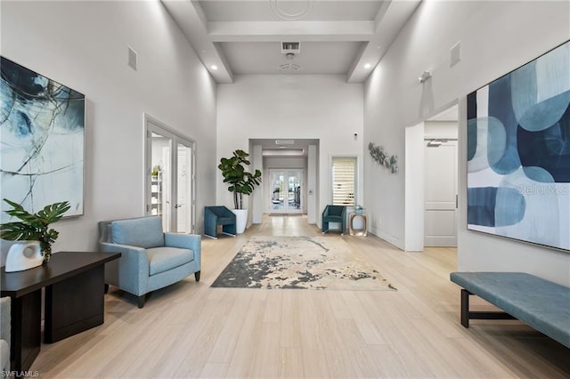 sitting room featuring visible vents, french doors, light wood-type flooring, and a towering ceiling