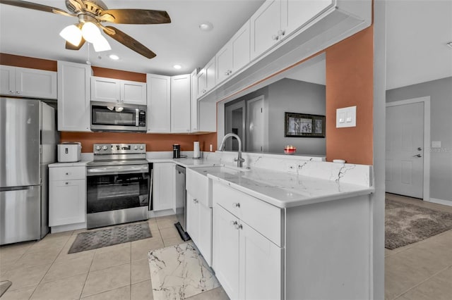 kitchen with light tile patterned floors, white cabinets, appliances with stainless steel finishes, a peninsula, and light stone countertops