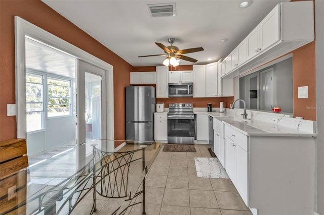 kitchen featuring appliances with stainless steel finishes, white cabinets, light tile patterned flooring, ceiling fan, and light stone countertops