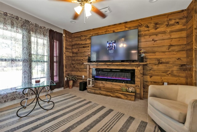 tiled living room with ceiling fan, a glass covered fireplace, wood walls, and visible vents