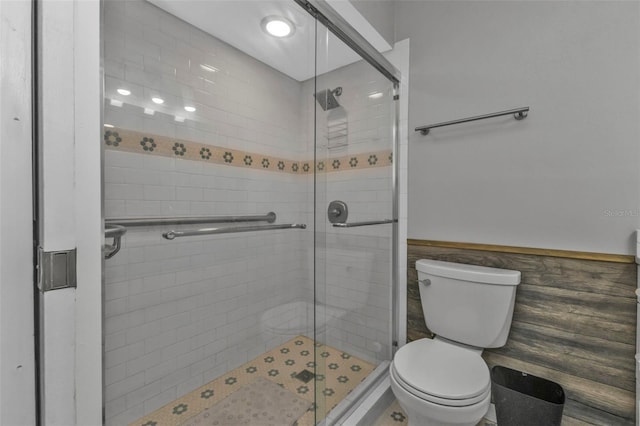 full bath with wainscoting, a stall shower, toilet, and tile walls