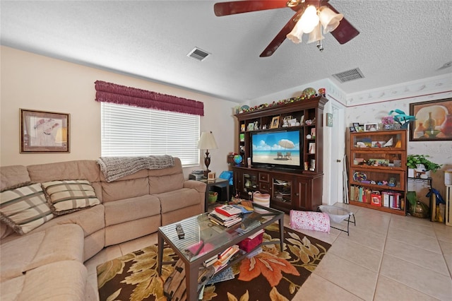 living room with tile patterned flooring, visible vents, ceiling fan, and a textured ceiling