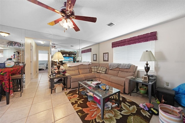 living room featuring light tile patterned floors, ceiling fan, visible vents, and a textured ceiling